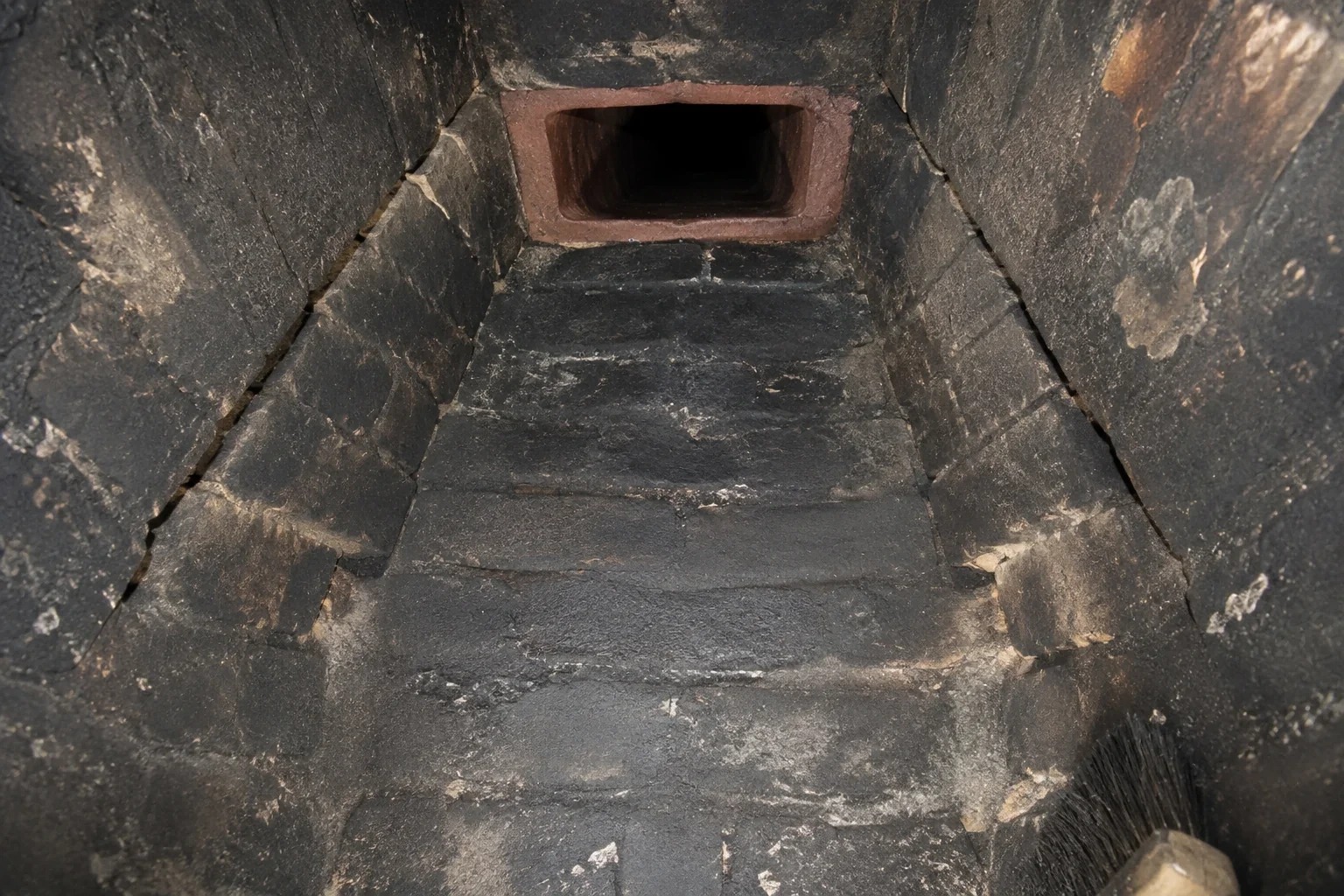 Illustration: Soot-darkened tapered masonry chamber leading to a terracotta flue opening.